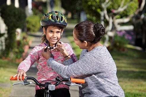 Adult woman checking the helmet of a girl seated on a bicycle
