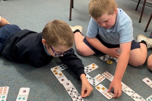 Two students in school uniforms lean over an array of cards on the floor