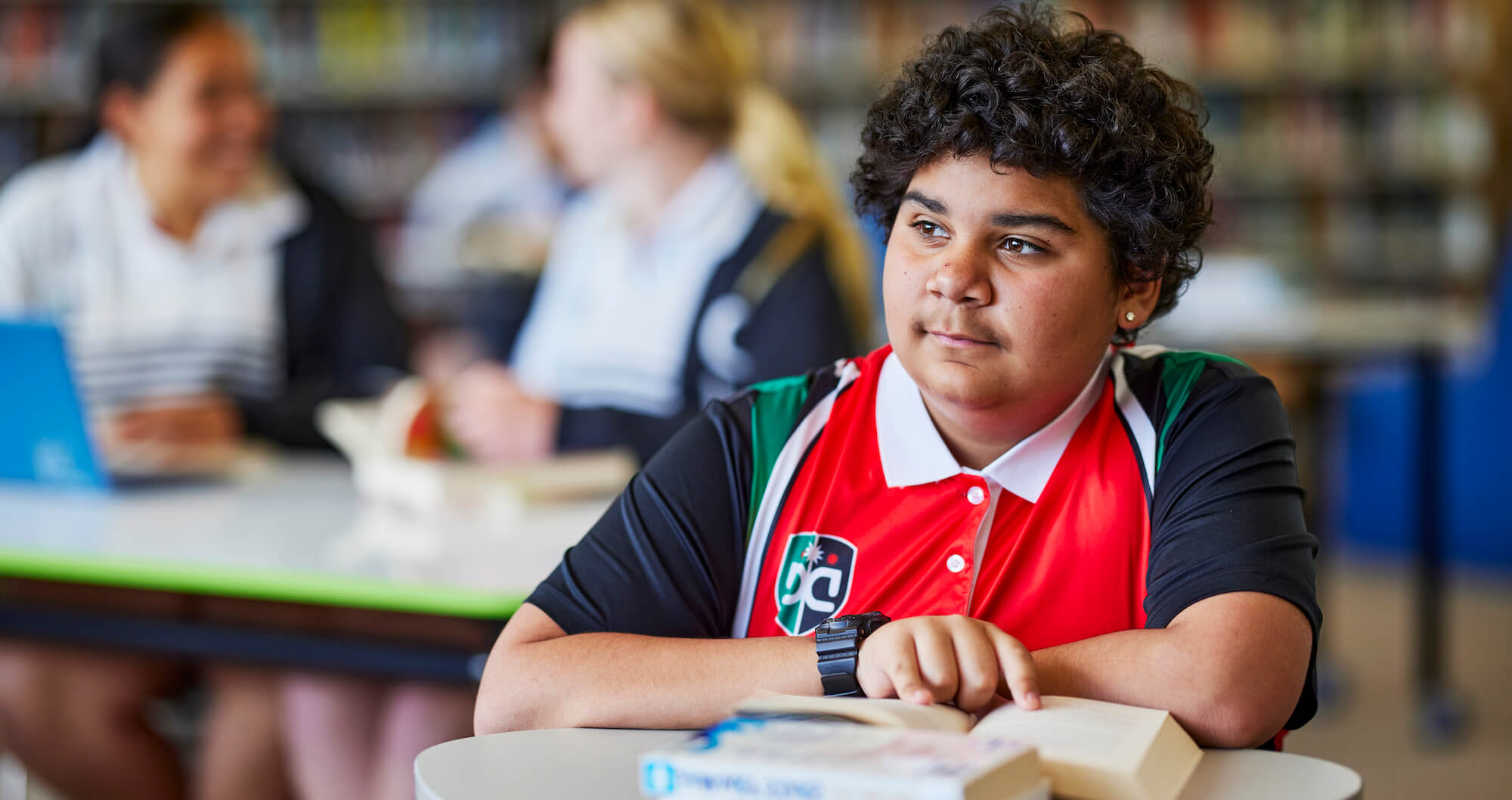 Teacher sitting at desk with students and helping them.