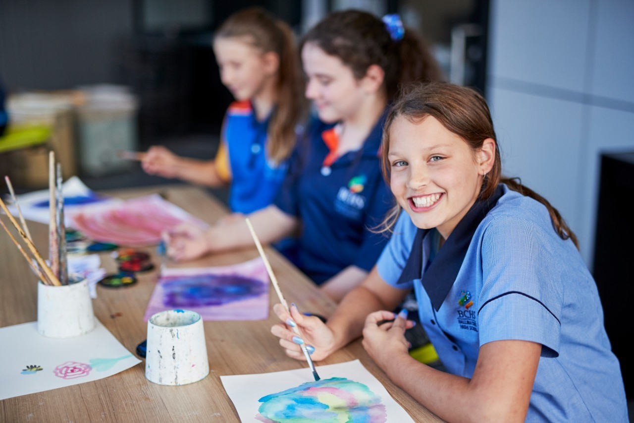 Three female students at a desk in art class painting with watercolour paint