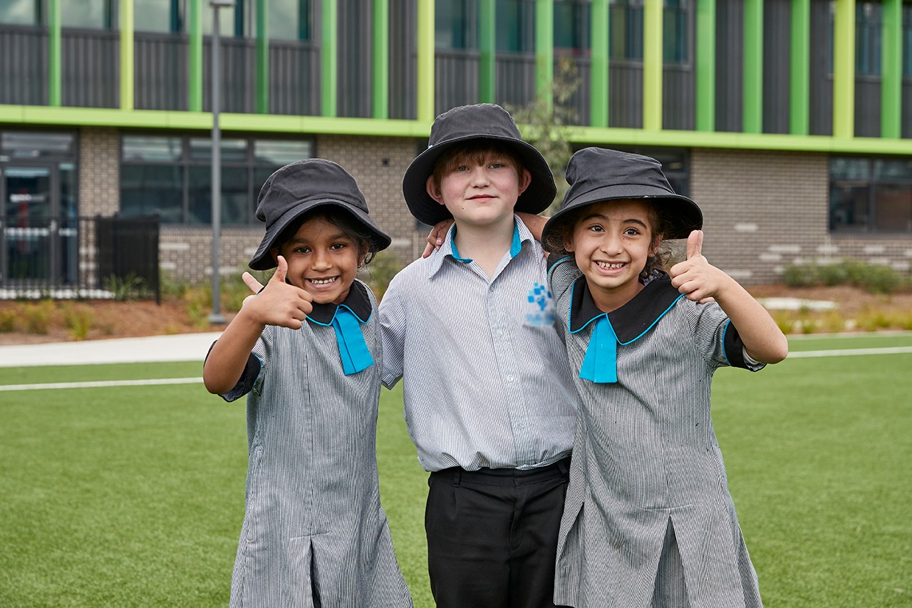 Three primary school students, two girls and one boy, with hats giving the thumbs up