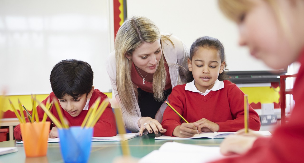 Image of female primary school teacher with two students at a desk