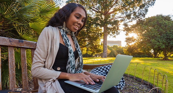 Female sitting in a park working on a laptop.