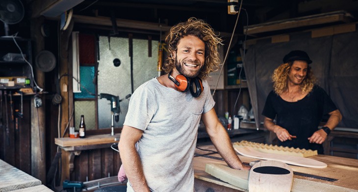 2 male carpenters with long hair making surfboards.