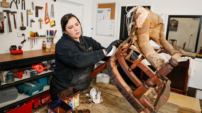 Female carpentry apprentice restoring wooden chair