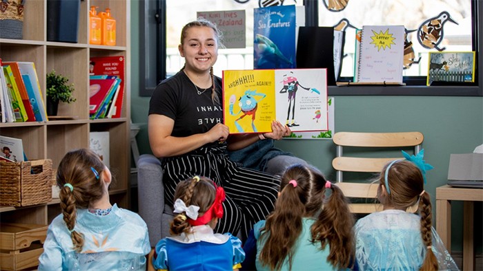Female trainee in early childhood care showing book illustrations to children.