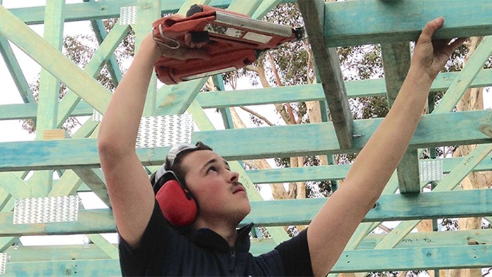 A young male apprentice builder working with nail gun.