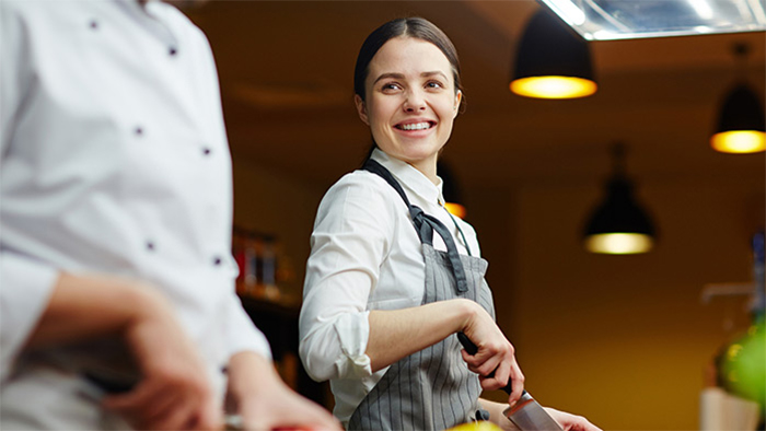 Smiling female hospitality apprentice in commercial kitchen