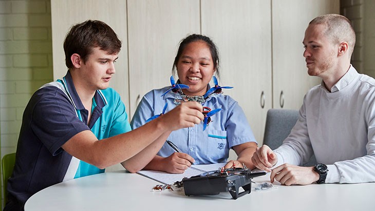 High school students working at desk holding a robotic device with male teacher