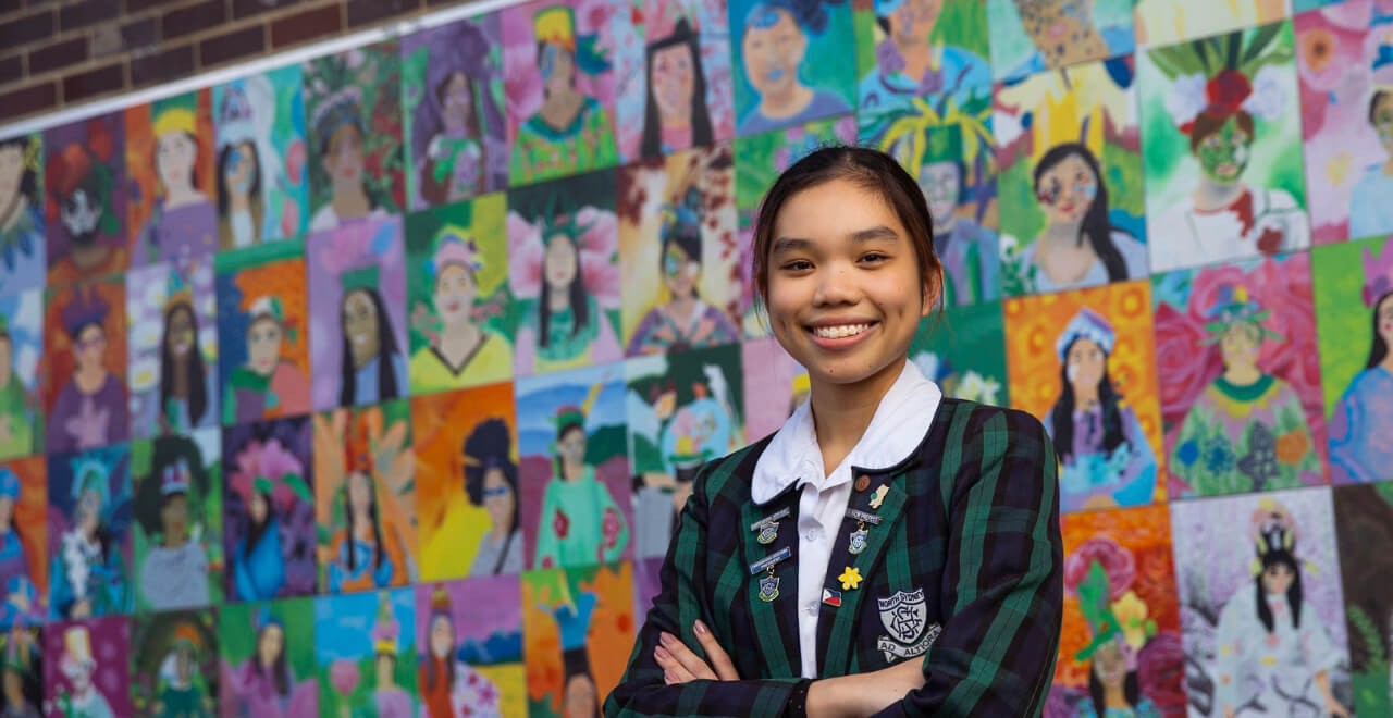 Student smiling standing in front of a mural. 