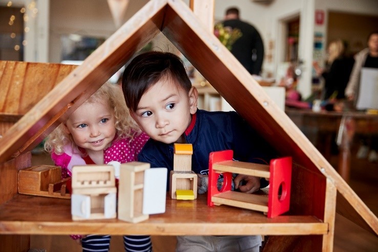 Two young children looking through a childrens dollhouse