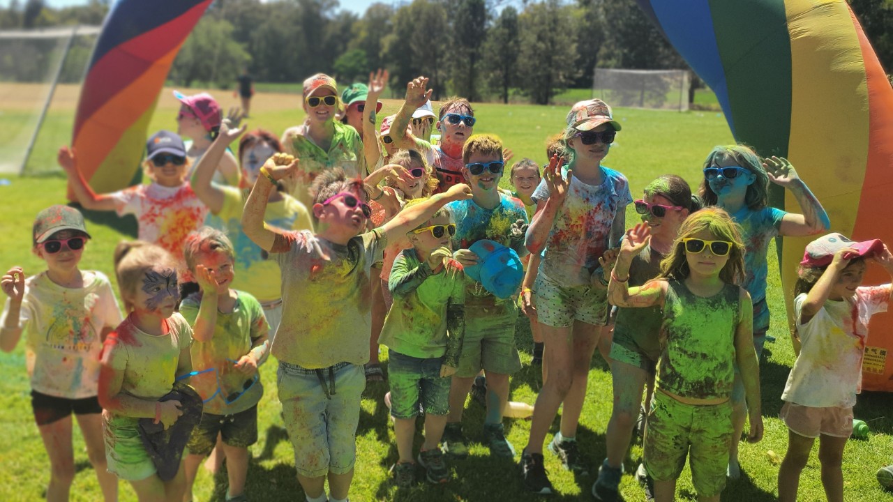 Kids at Eugowra Public School standing under inflatable rainbow covered in pigment from colour run.