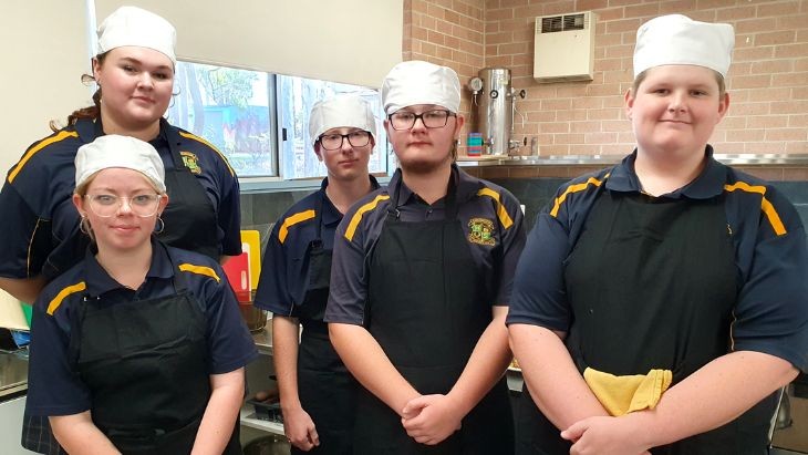 Five students wearing aprons and chef hats.