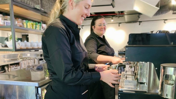 Two women working at a barista machine.